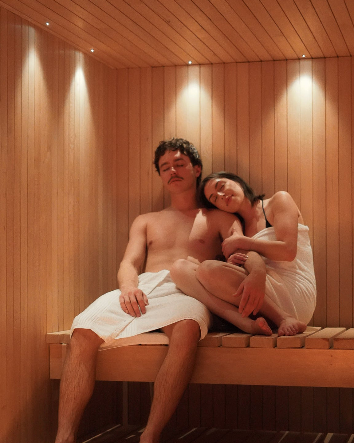 Two people sitting together in a wooden sauna.