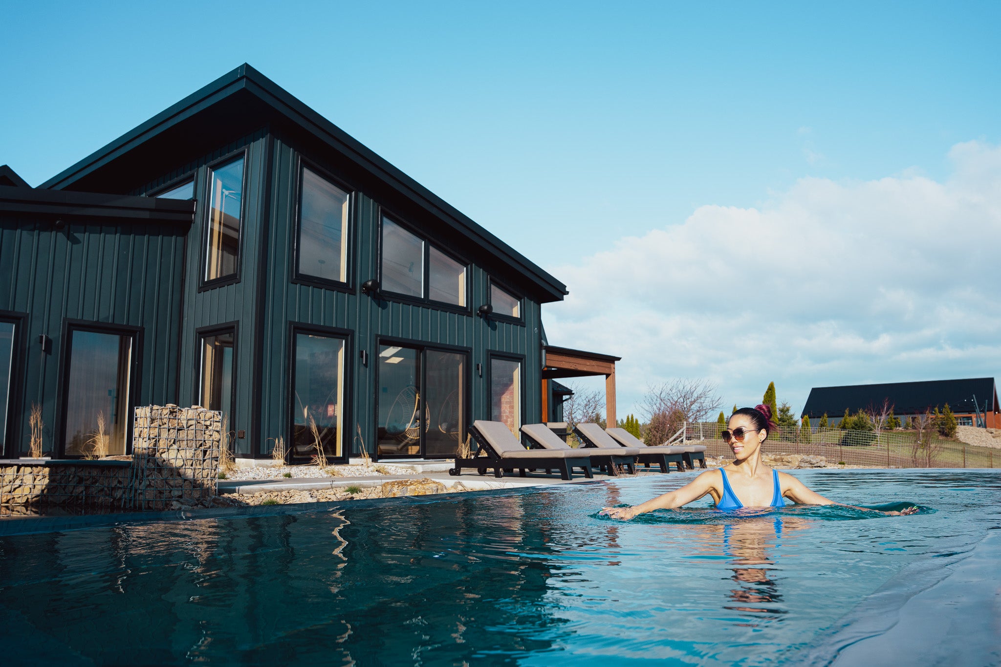 Woman in a thermal infinity pool with a modern house and clear sky in the background