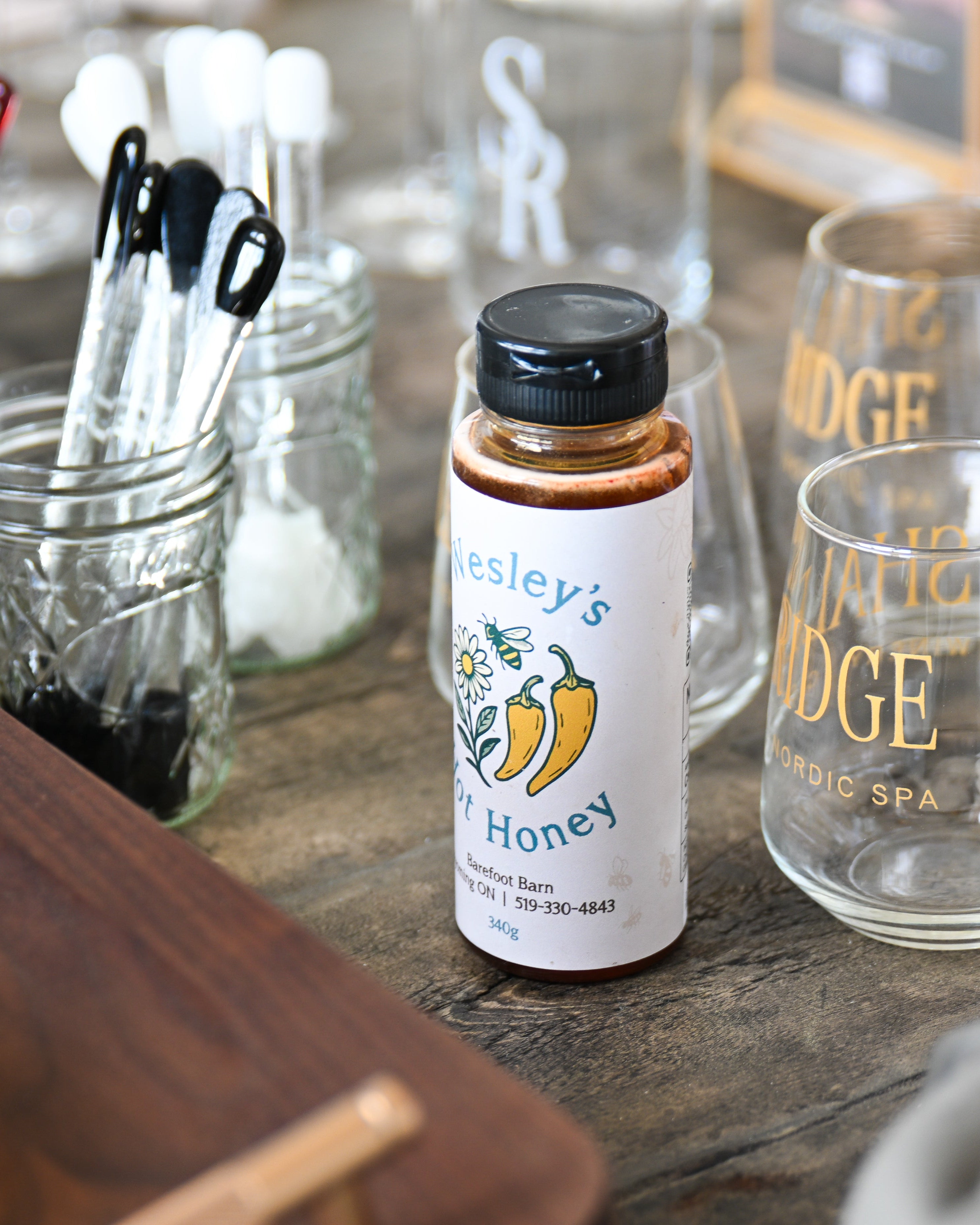 Bottle of Wesley's Hot Honey on a wooden surface with glasses and utensils in the background