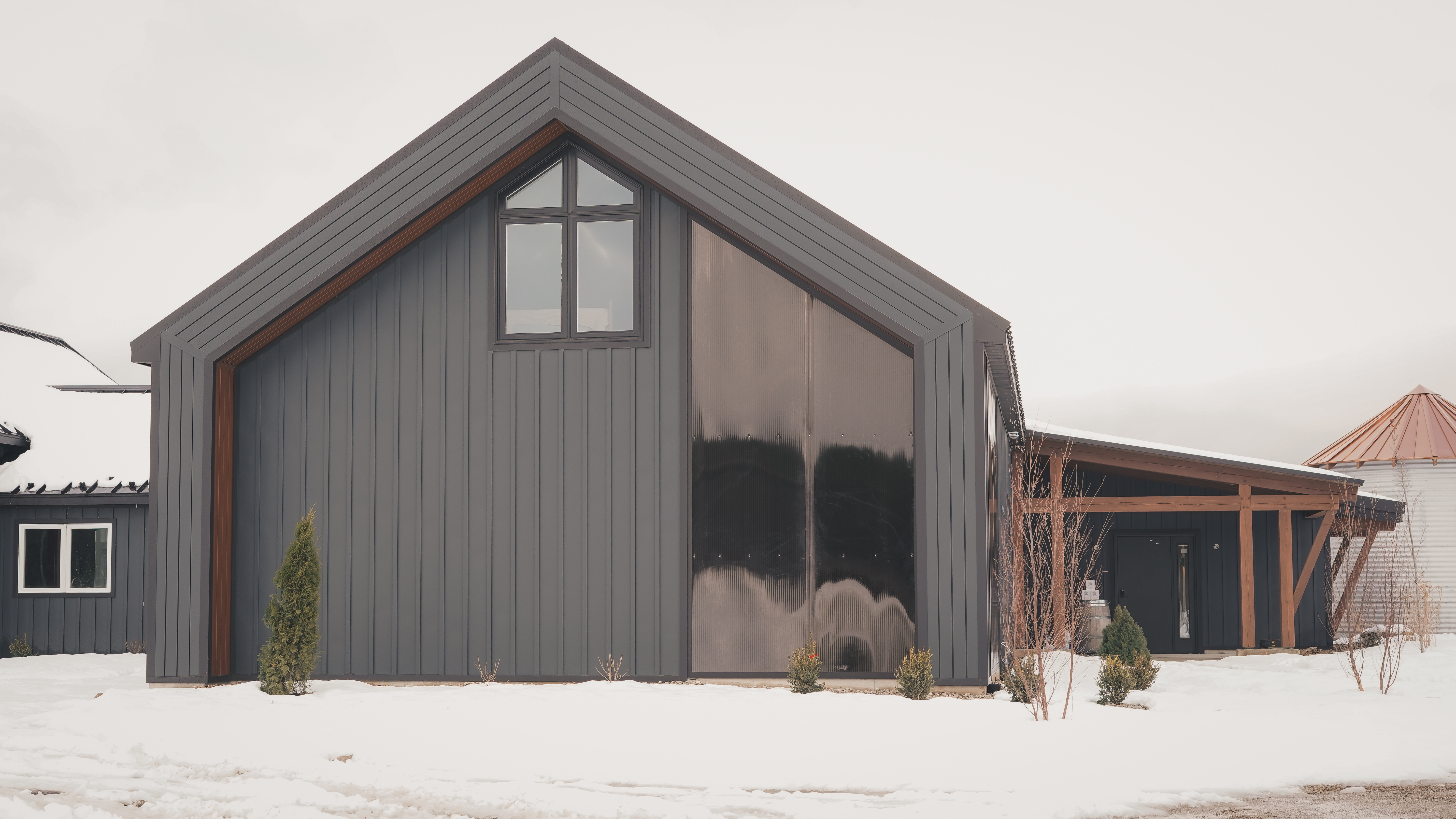 Front view of a modern matte black gabled building with large glass inserts in a snowy landscape.