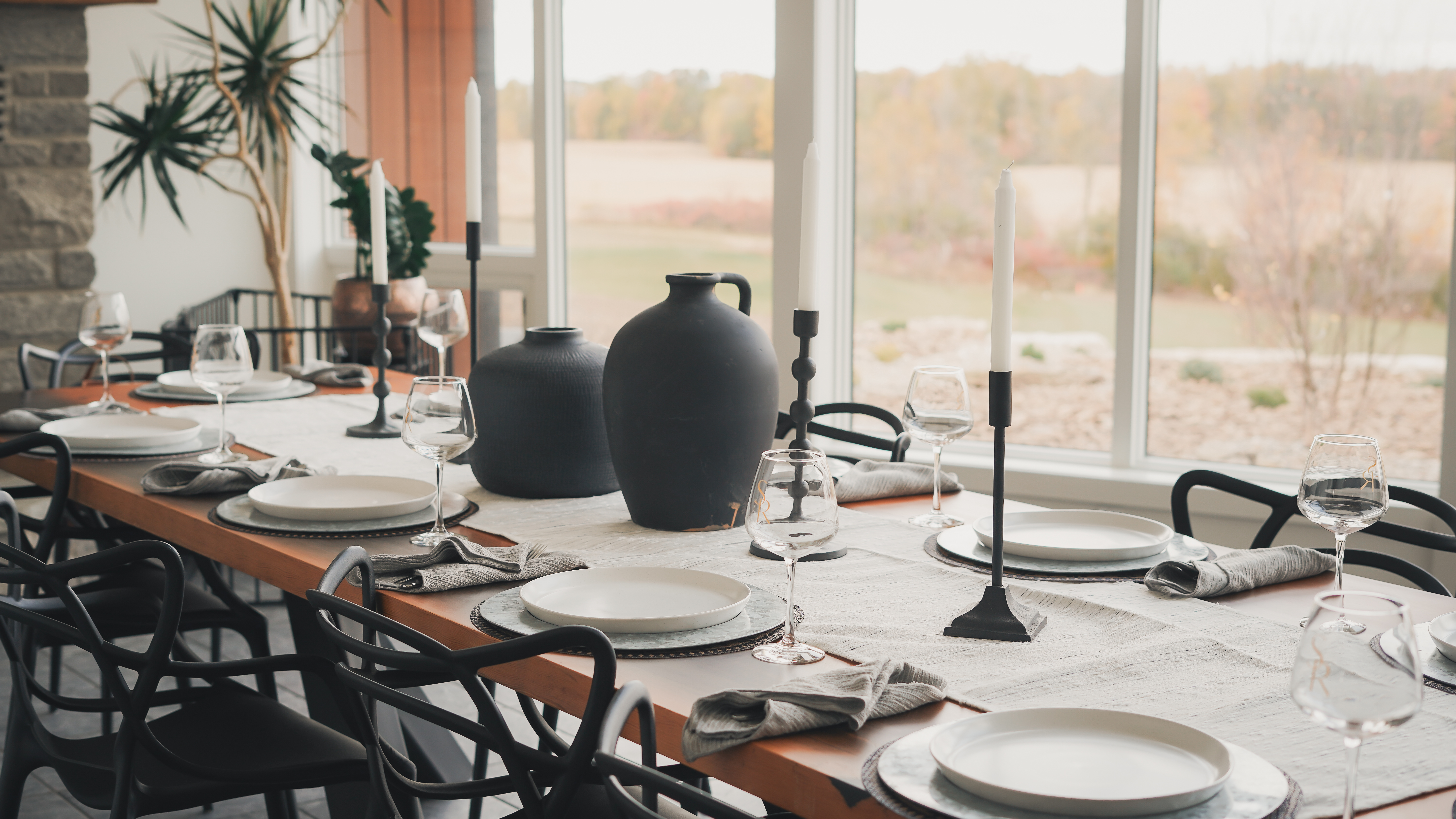 Formal dining table setting with wine bottles, tall white candles in black holders, and white plates.