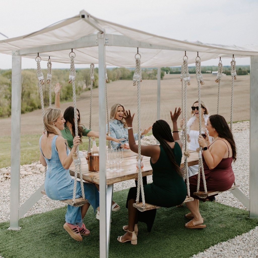 Group of women enjoying drinks at outdoor swing table overlooking Ontario countryside